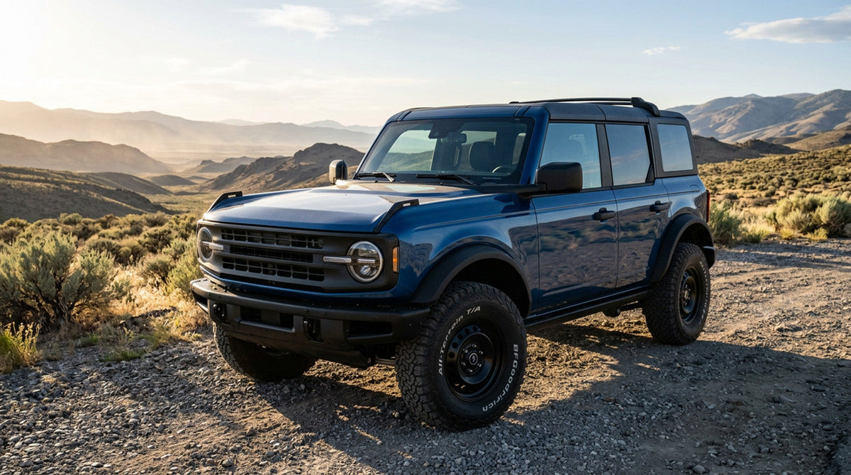 A dark blue Ford Bronco parked on a gravel pullout in the high desert, photographed from a low front three-quarter angle with the hood in the foreground