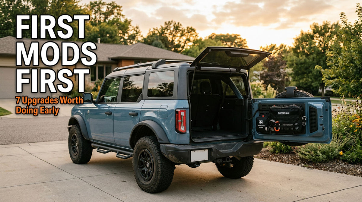 A blue four-door Ford Bronco parked in a driveway at sunset with the rear swing gate open and a gear organizer bag mounted to it, side steps fitted, under a headline reading First Mods First, 7 Upgrades Worth Doing Early