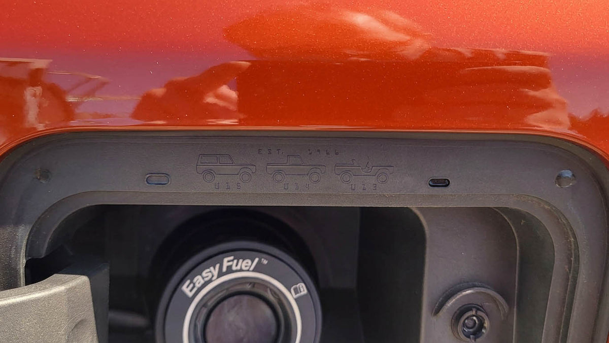 Open fuel door on an orange Ford Bronco showing the embossed EST. 1966 Easter egg with U15 wagon, U14 half cab and U13 roadster silhouettes above the Easy Fuel capless filler