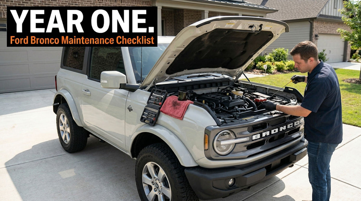 A white two-door Ford Bronco parked in a suburban driveway with the hood raised while a man in a navy shirt checks the oil dipstick, a red shop rag draped over the engine bay, under a headline reading Year One, Ford Bronco Maintenance Checklist