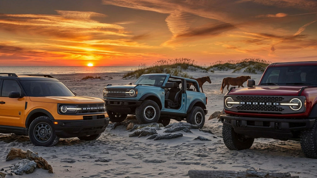 Three Ford Broncos parked on a beach at sunset: an orange Bronco Sport, a light blue two door Bronco with its doors and roof removed, and a dark red four door Bronco, with two wild horses on the dunes behind them