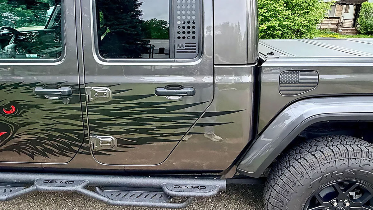 Subdued American flag vinyl decal on the fuel door of a gray Jeep Gladiator, with a feather graphic running across the doors