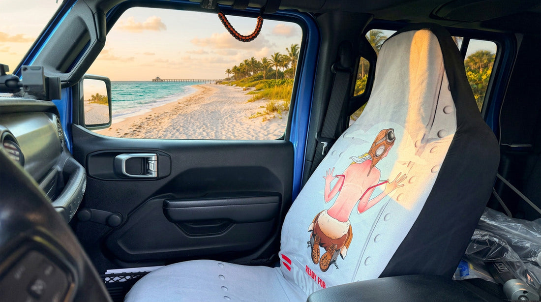 Ready for Takeoff pin-up aviator seat cover installed on the passenger seat of a blue Jeep parked at the beach at sunset
