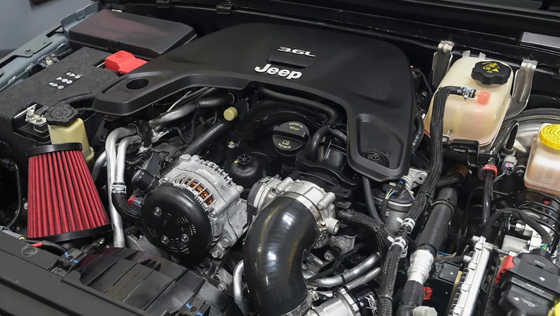 A hand lifting the paper cartridge oil filter from its housing on top of a Jeep Wrangler 3.6L Pentastar engine