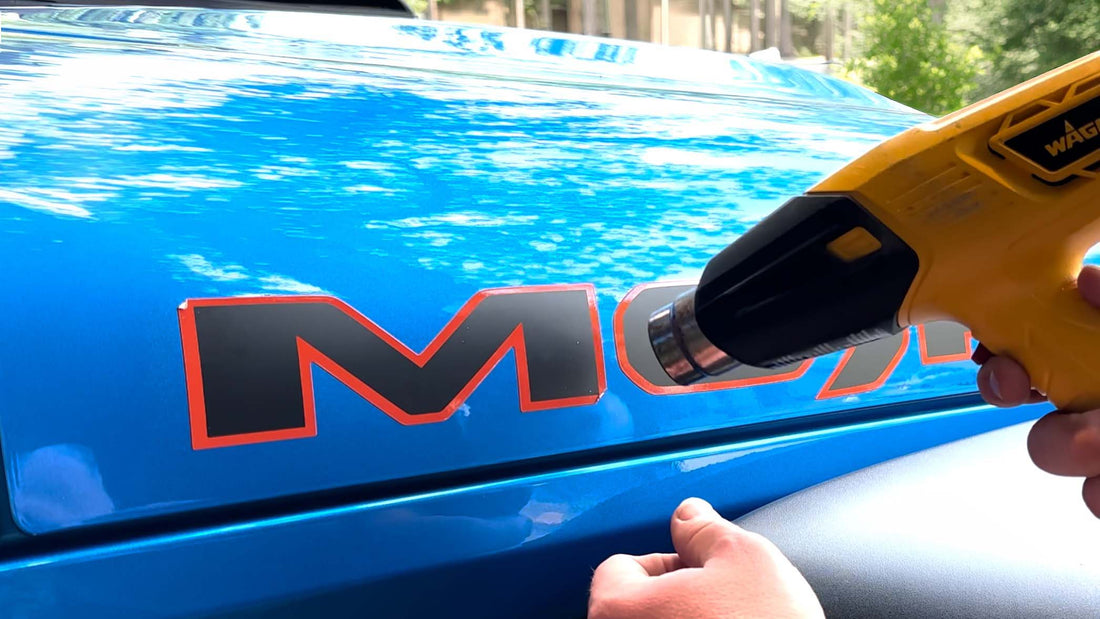 Person removing a Jeep decal with heat gun without damaging paint