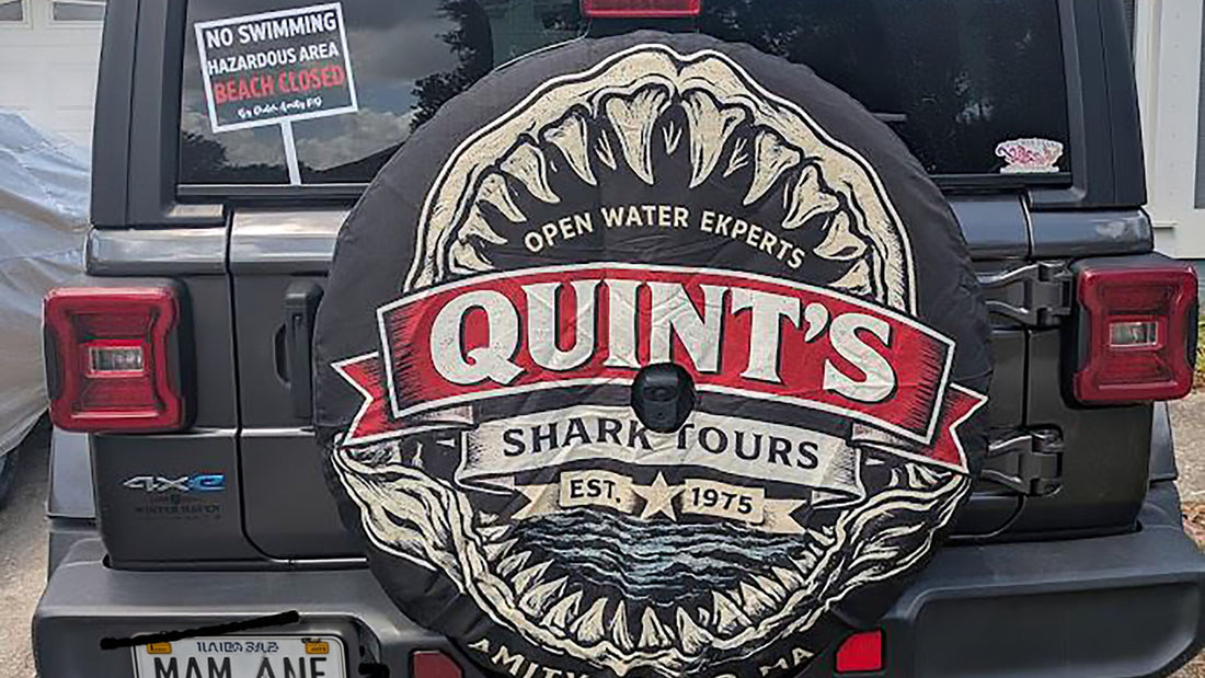 Soft vinyl spare tire cover with a black and red shark tour design and backup camera opening, mounted on a gray Jeep Wrangler JL
