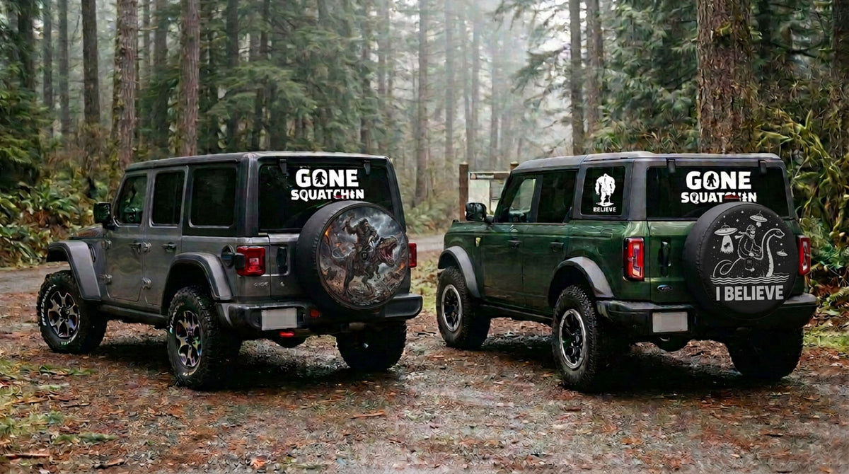 Gone Squatchin Bigfoot decals on the rear windows of a Jeep Wrangler and a Ford Bronco parked at a forest trailhead, with Bigfoot spare tire covers mounted on both