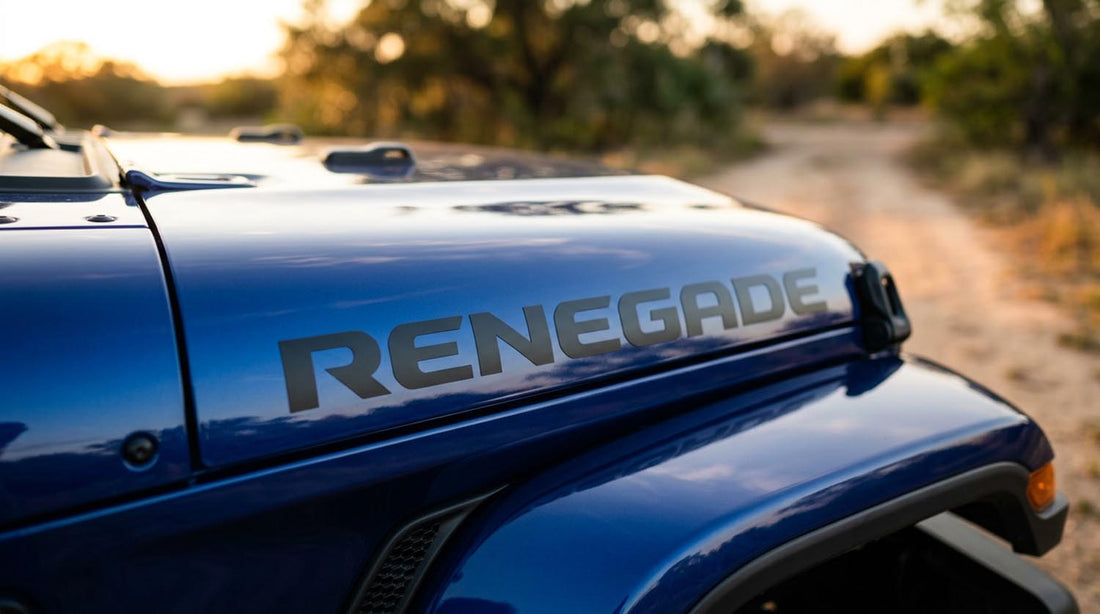 Black RENEGADE hood lettering on the glossy blue side hood of a Jeep Wrangler on a dirt trail at sunset