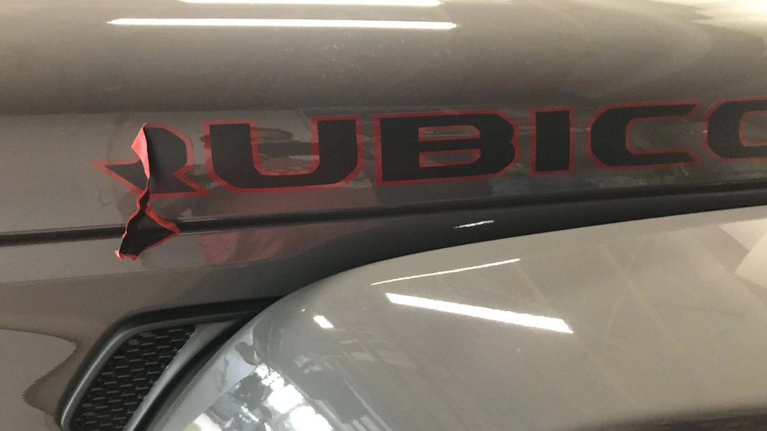 Factory RUBICON hood decal on a gray Jeep Wrangler with the black and red vinyl lifted and torn at one edge