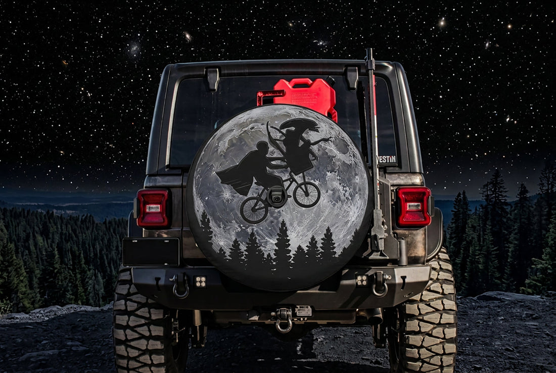 80s Sci-Fi Parody Mashup Moon spare tire cover on a Jeep Wrangler at night: a caped rider pedals a bicycle across a full moon with a long-headed alien in the front basket, pine trees below, backup camera hole in the center