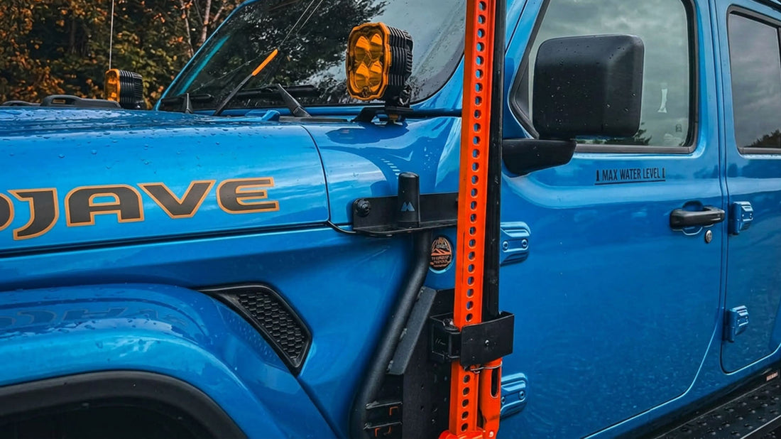 Orange Hi-Lift jack mounted to the side of a blue Jeep Wrangler