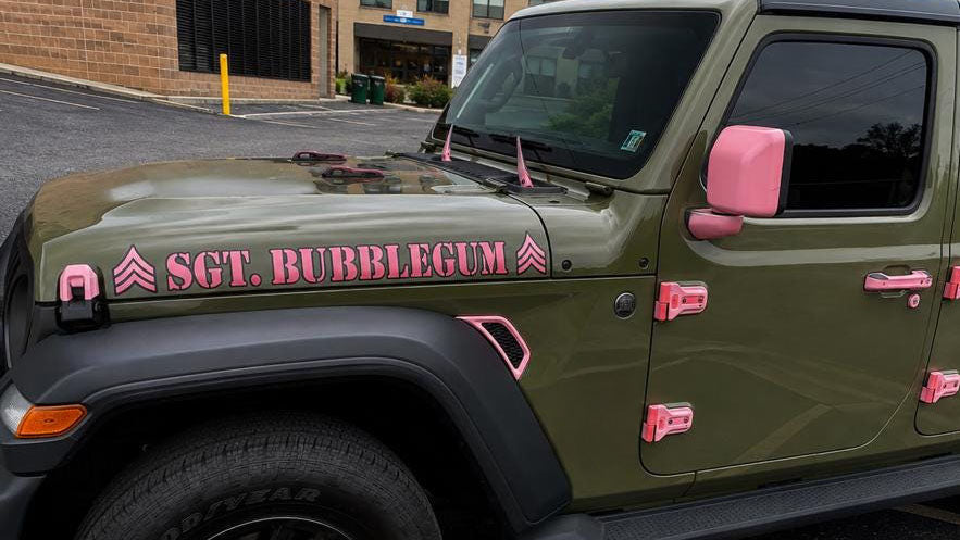 Pink SGT. BUBBLEGUM custom hood lettering with military rank chevrons on the olive green hood of a Jeep Gladiator JT with pink mirror caps, hinges and door handles