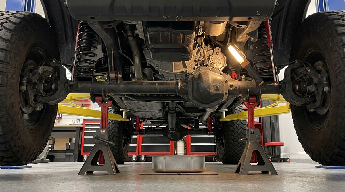 Underside of a lifted Jeep on jack stands with a drain pan below the drivetrain
