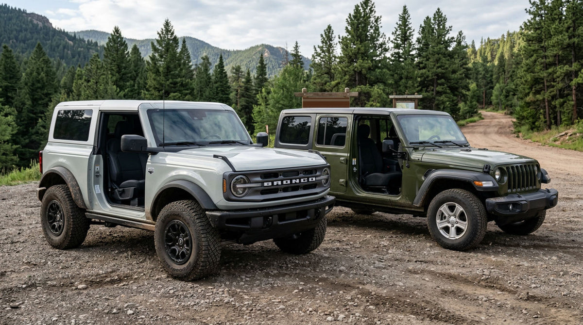 Ford Bronco and olive green Jeep Wrangler JLU parked side by side at a mountain trailhead with their front doors removed, both still carrying side mirrors mounted ahead of the door opening