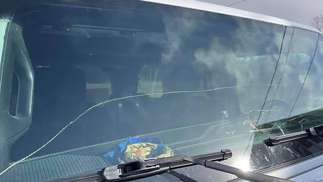 Long horizontal crack running the full width of a Jeep Wrangler windshield, seen across the hood with the wiper blades parked at the base of the glass