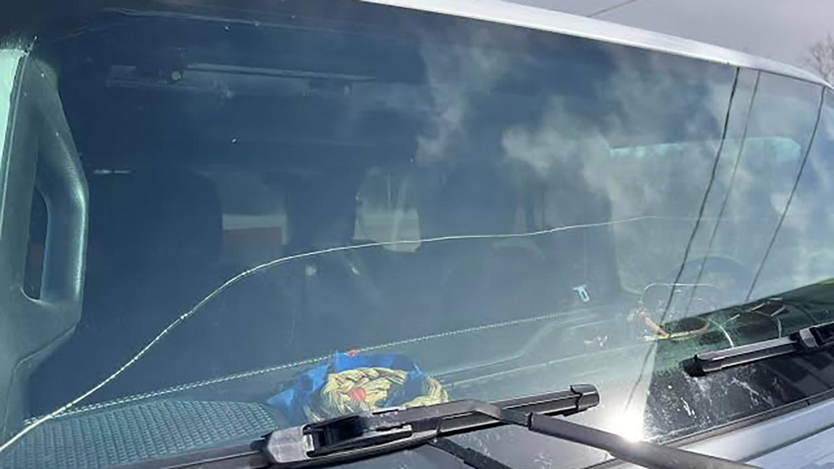 Long horizontal crack running the full width of a Jeep Wrangler windshield, seen across the hood with the wiper blades parked at the base of the glass
