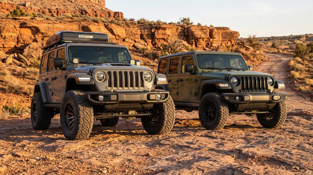 Dark green Jeep Wrangler Willys parked beside a silver Rubicon 392 with a rooftop tent on a red rock desert trail at sunset