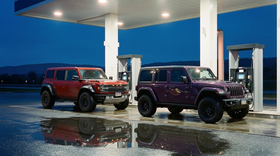 Ford Bronco Raptor and Jeep Wrangler 392 parked at fuel pumps under a lit station canopy at dusk