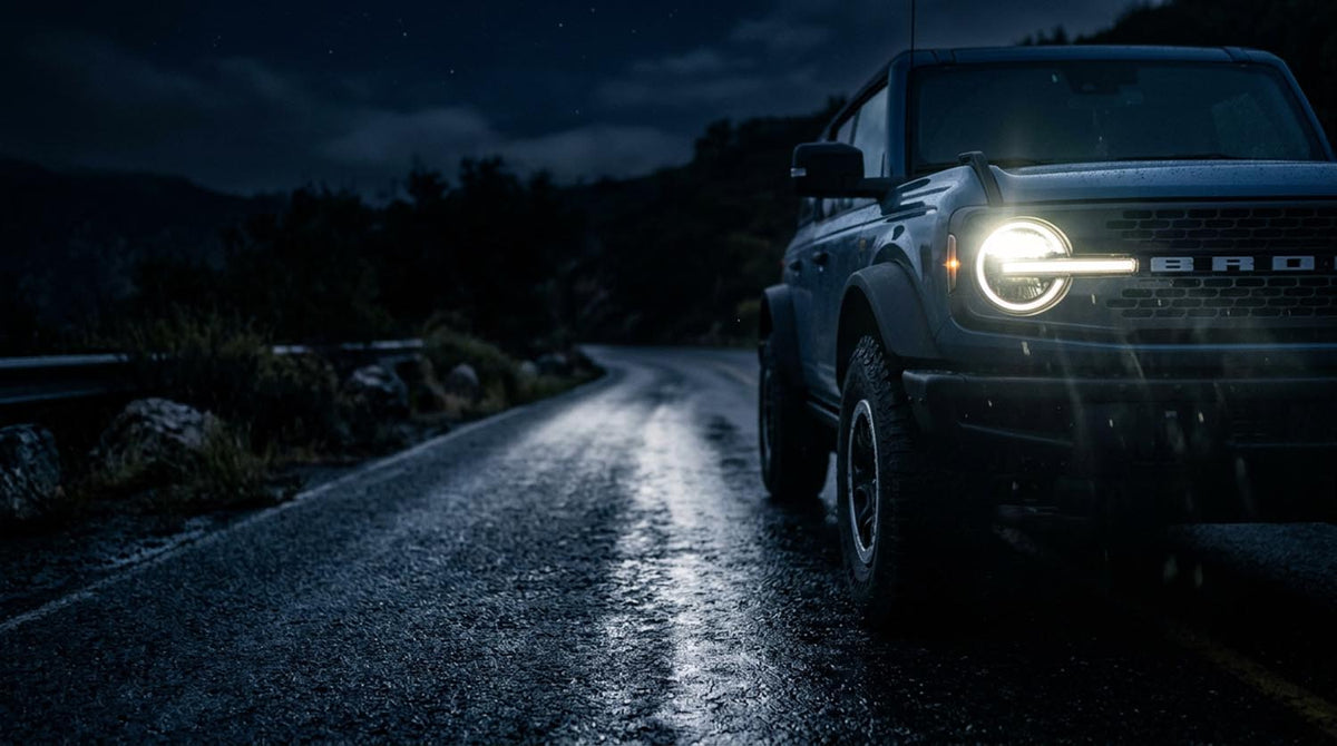 Ford Bronco headlights illuminating a wet mountain road at night