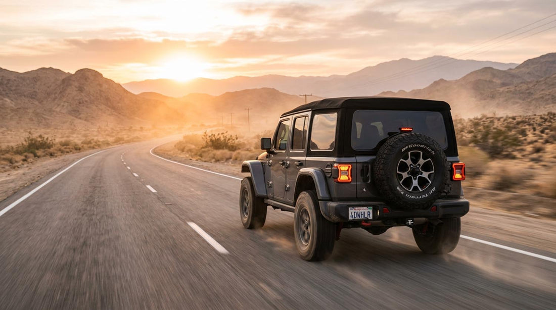 Jeep Wrangler with rear-mounted spare tire driving on a desert highway at sunset