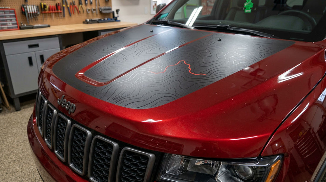 Custom matte black topographic contour hood decal with a red accent line on a red Jeep Grand Cherokee WK2, photographed in a garage