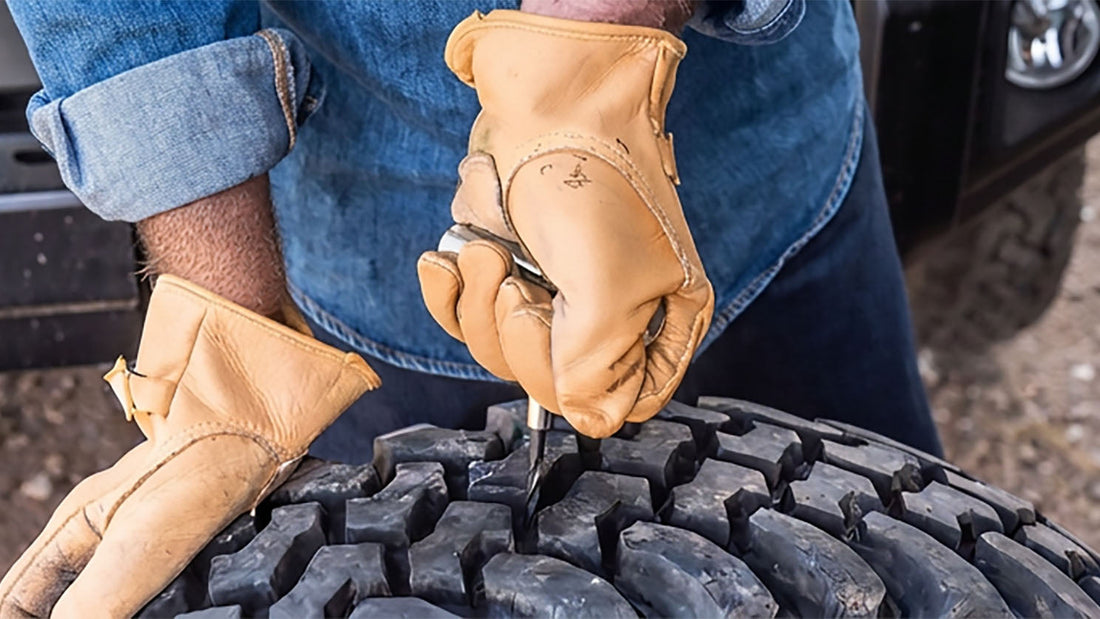 Gloved hands using an insertion tool to install a tire plug in the tread of a mud-terrain off-road tire