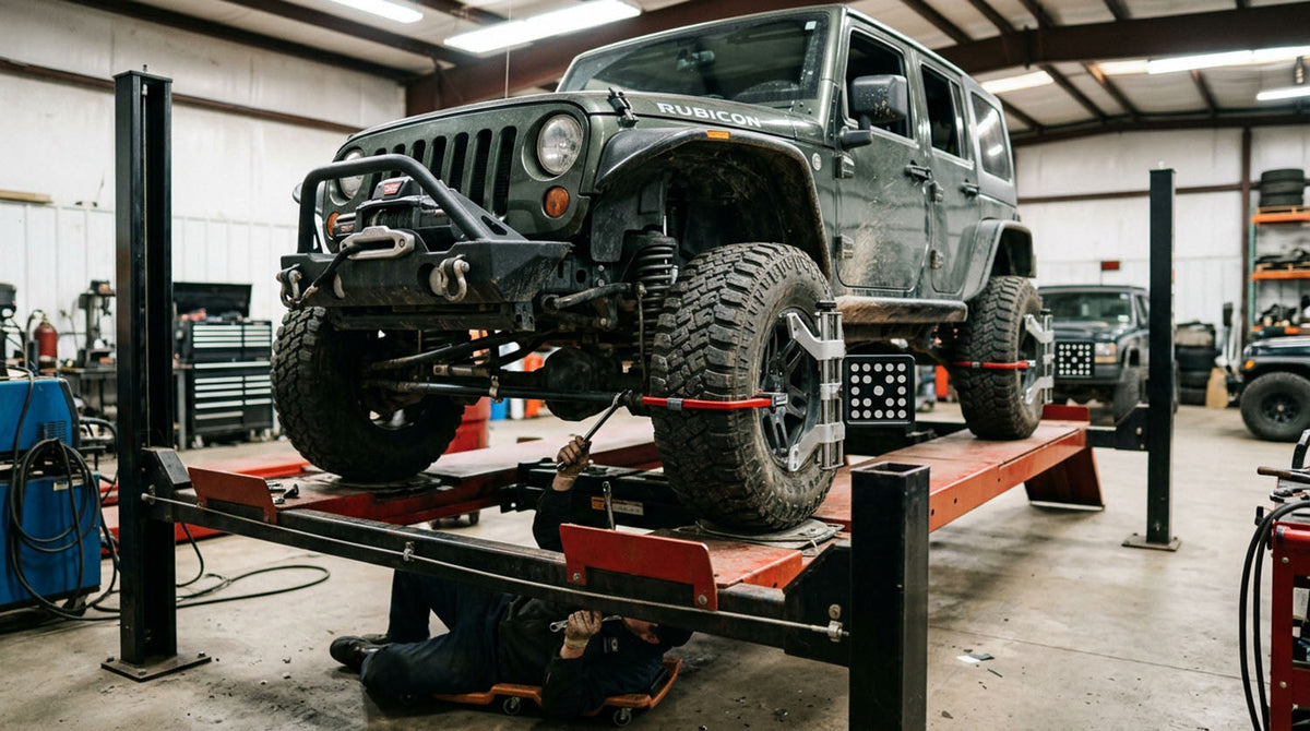 Lifted Jeep Wrangler on an alignment rack in an off-road shop with a technician adjusting the suspension