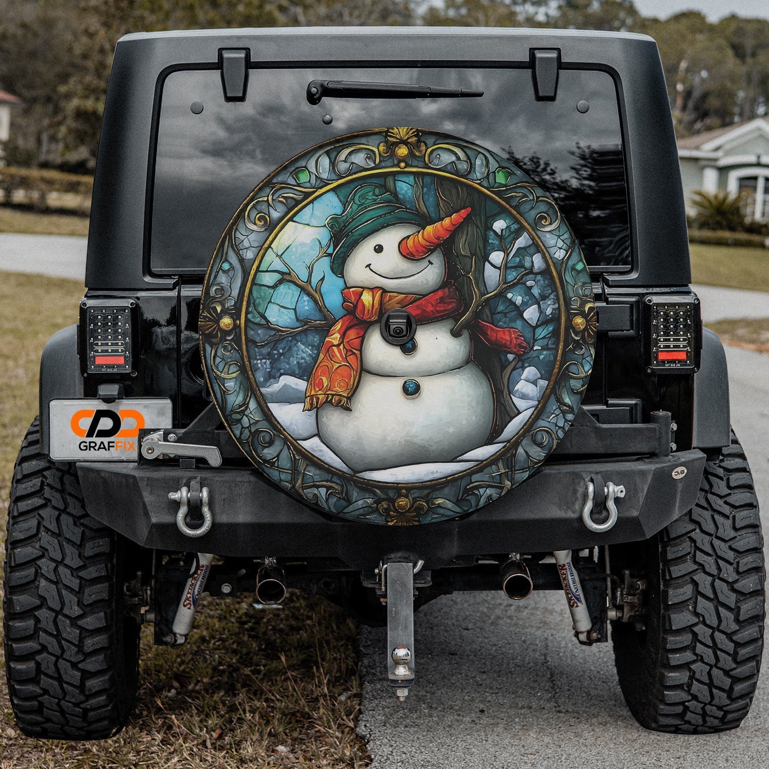 Black Jeep Wrangler showing stained glass snowman tire cover and GRAFFIX plate badge driveway scene