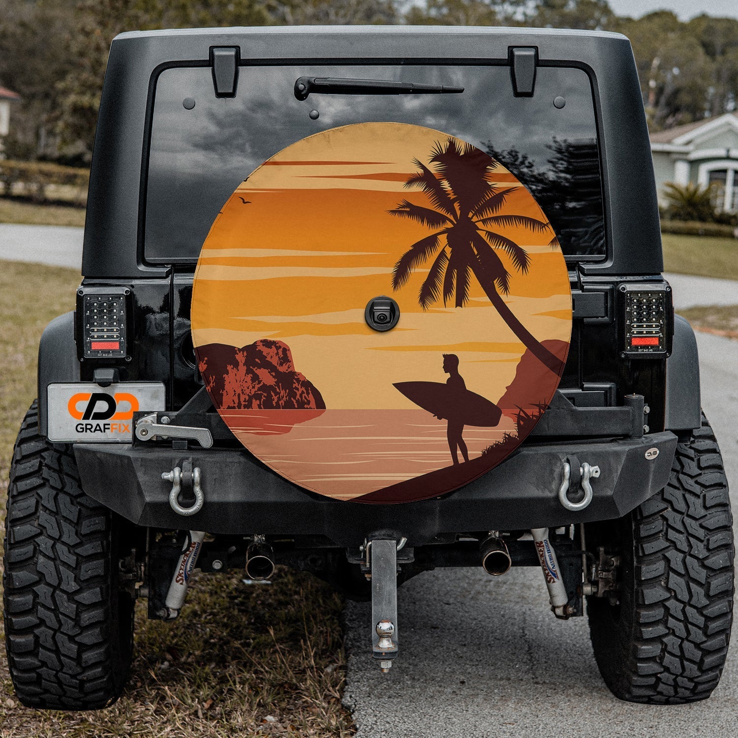 Sunset surfer tire cover on red Jeep Wrangler showing orange sky, palm tree, and lone surfer silhouette scene