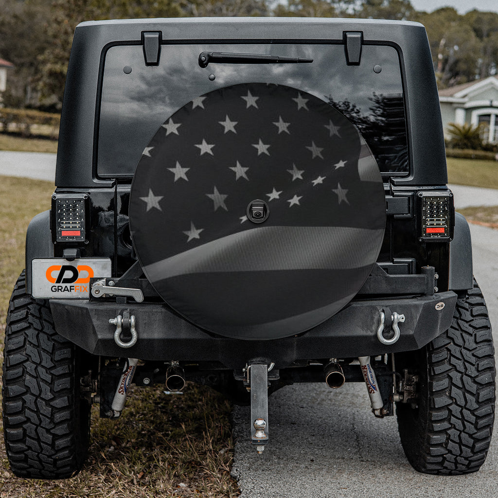 Wavey No Quarter American flag spare tire cover on black Jeep Wrangler with Graffix plate in driveway setting
