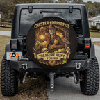 a black Jeep Wrangler with a large round spare tire cover on the rear of the vehicle. The cover has an illustration of a man in a safari hat and holding a lantern, surrounded by treasure chests and other safari-themed items.