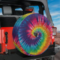 Rainbow spiral tie-dye spare tire cover mounted on red Jeep Wrangler rear with mountain horizon view