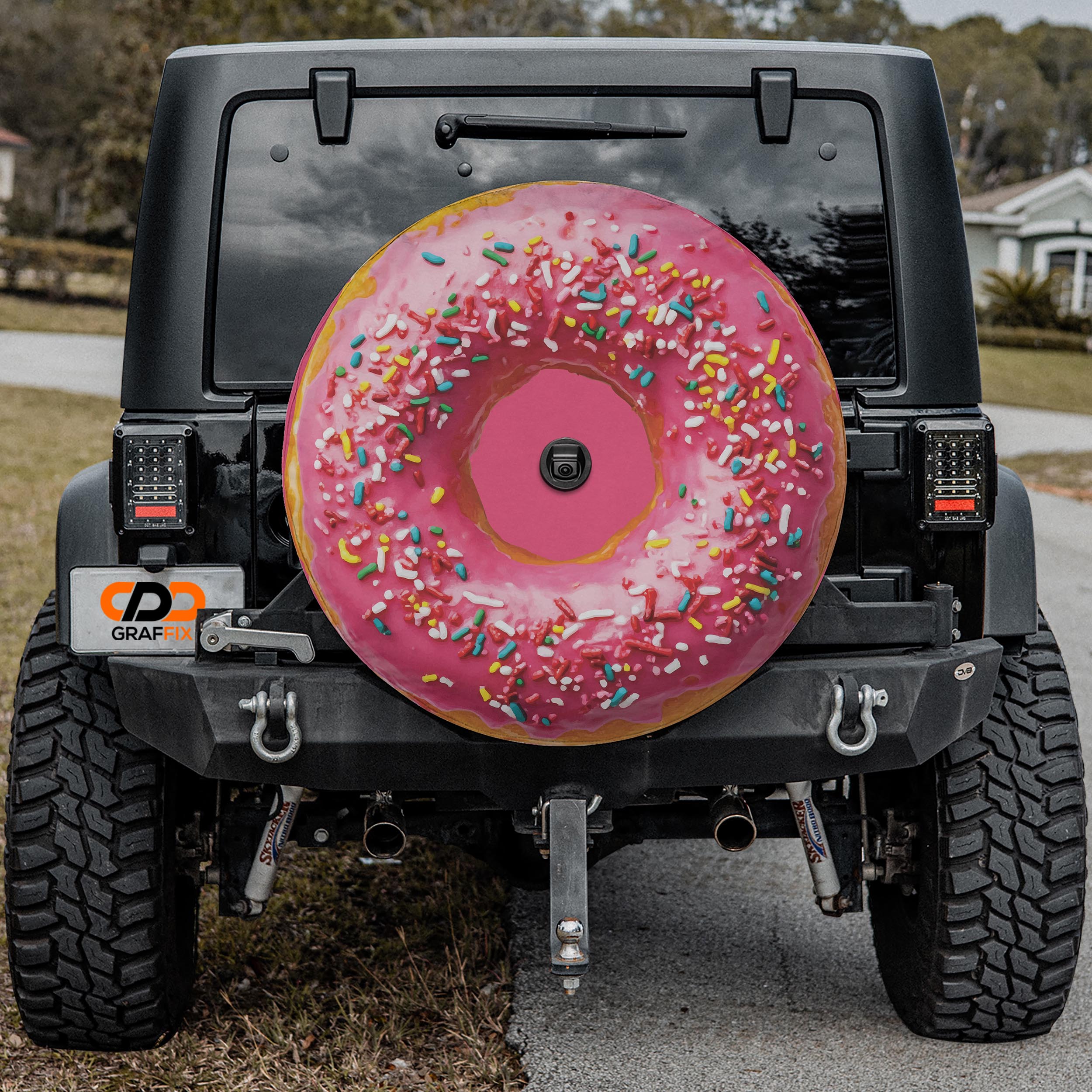 a black Jeep Wrangler with a large, colorful donut-shaped spare tire attached to the rear of the vehicle.