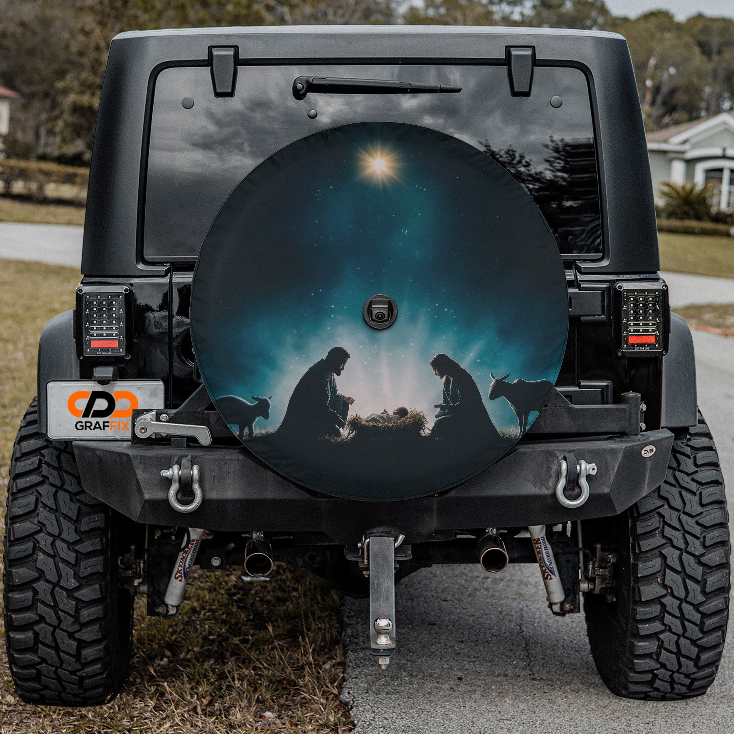 the back of a black Jeep Wrangler with a large, round spare tire cover featuring a nativity scene.