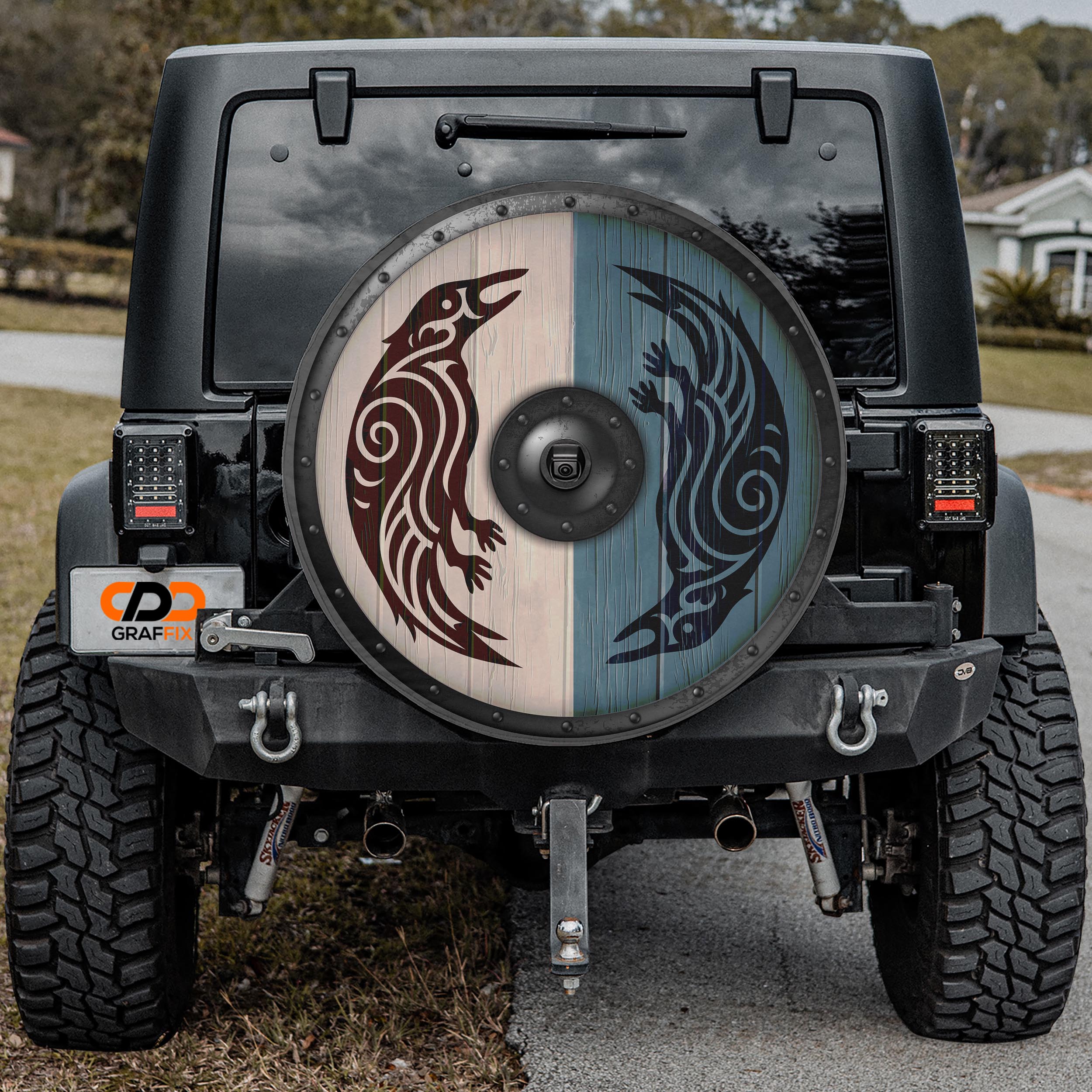 the back of a black Jeep Wrangler with a large, decorative wheel cover featuring a design of two stylized birds.