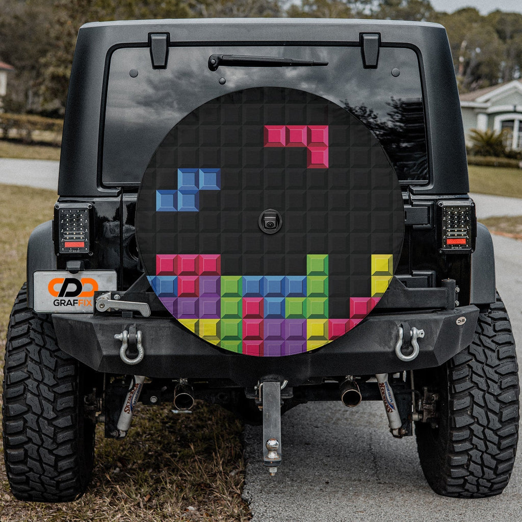 Pixel block puzzle tire cover on red Jeep Wrangler showing 8-bit gaming bricks with backup camera port