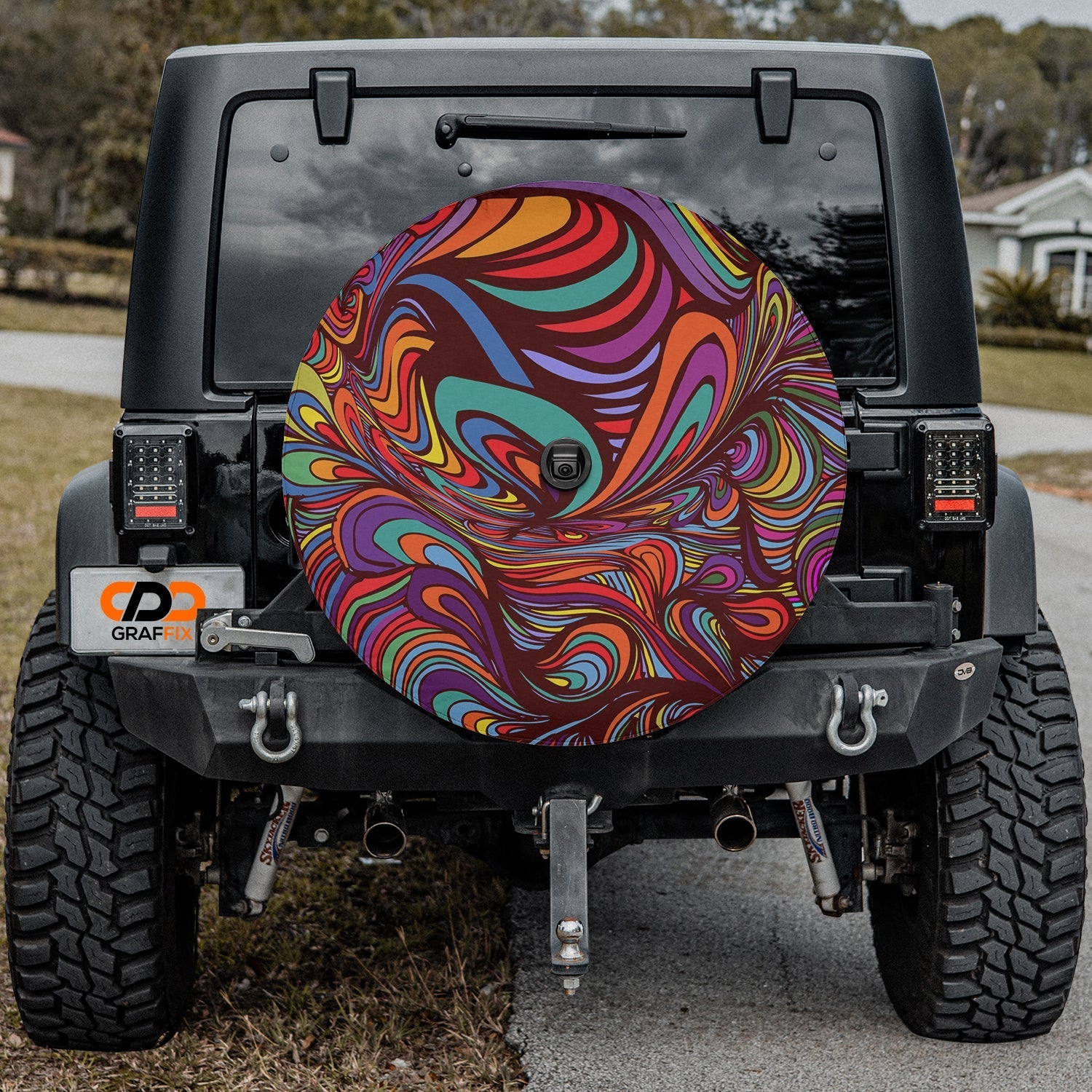 Psychedelic rainbow swirl tire cover on black Jeep Wrangler with neighborhood street and grass behind