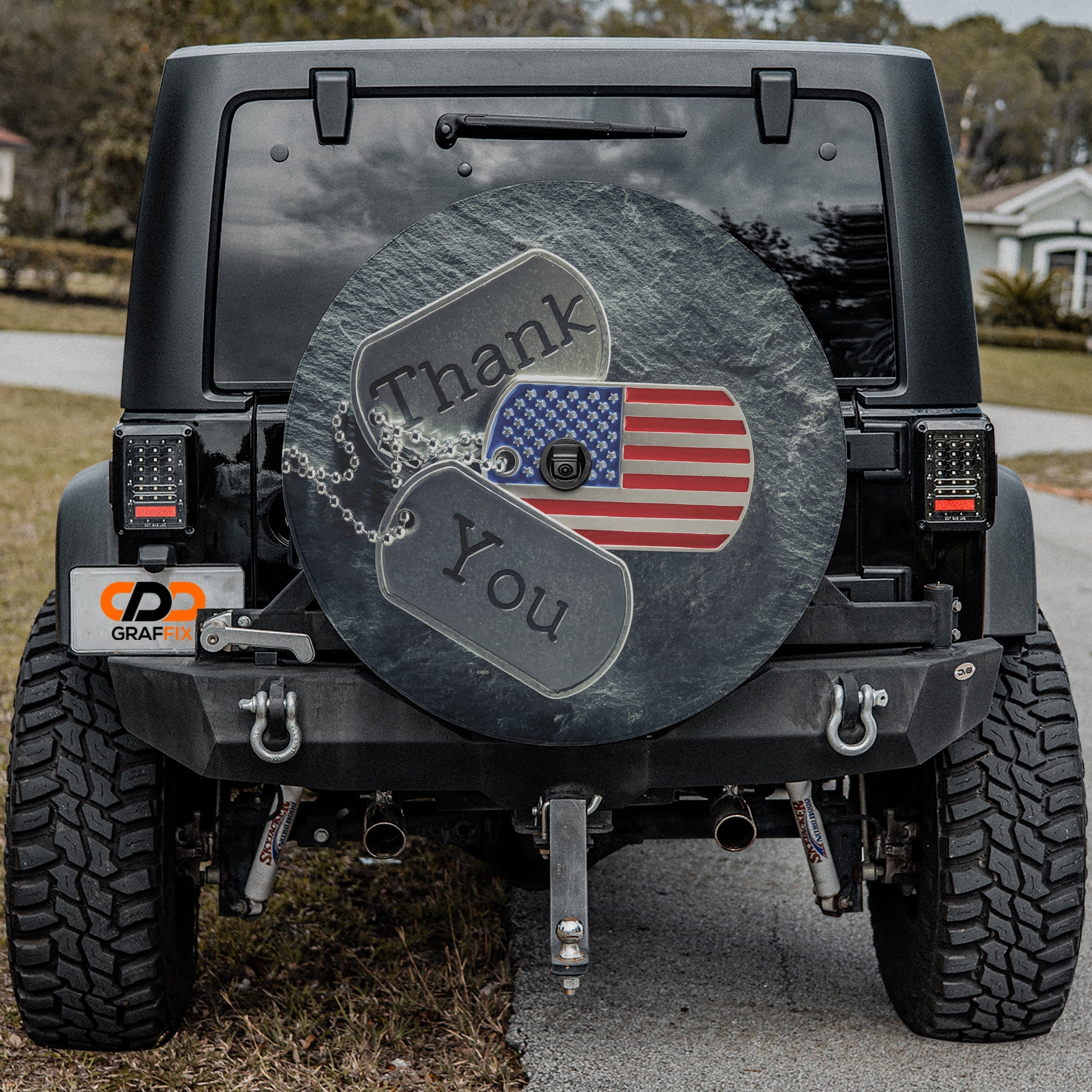 Veterans tribute dog tags Thank You spare tire cover installed on a red Jeep Wrangler tailgate in desert scene