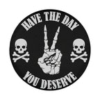 A black and white circular logo with the text "HAVE THE DAY YOU DESERVE" and two skull and crossbones symbols on either side.
