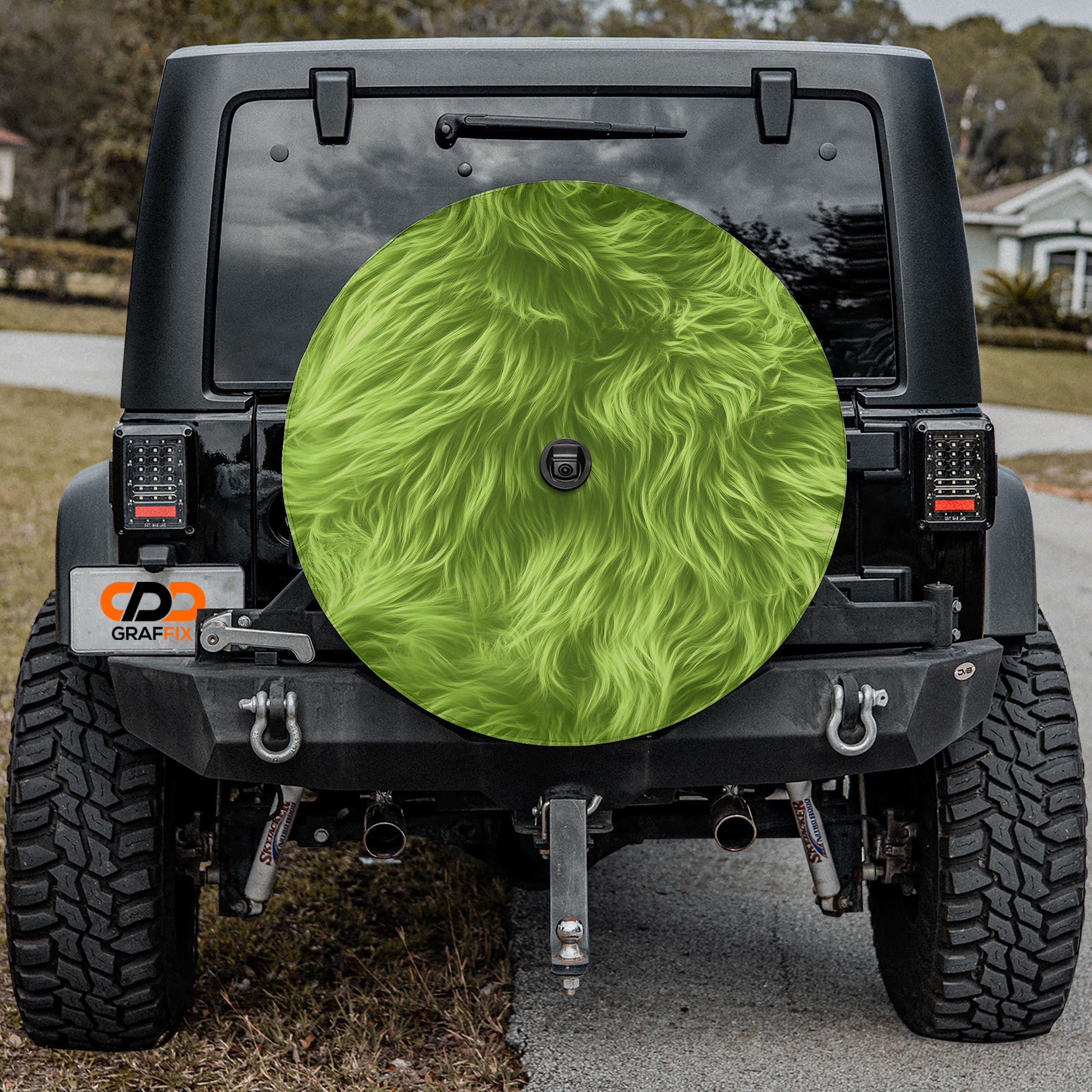 a black Jeep Wrangler with a large green fuzzy wheel cover attached to the rear of the vehicle.