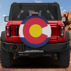 Colorado state flag spare tire cover mounted on red Ford Bronco rear with red rock canyon backdrop