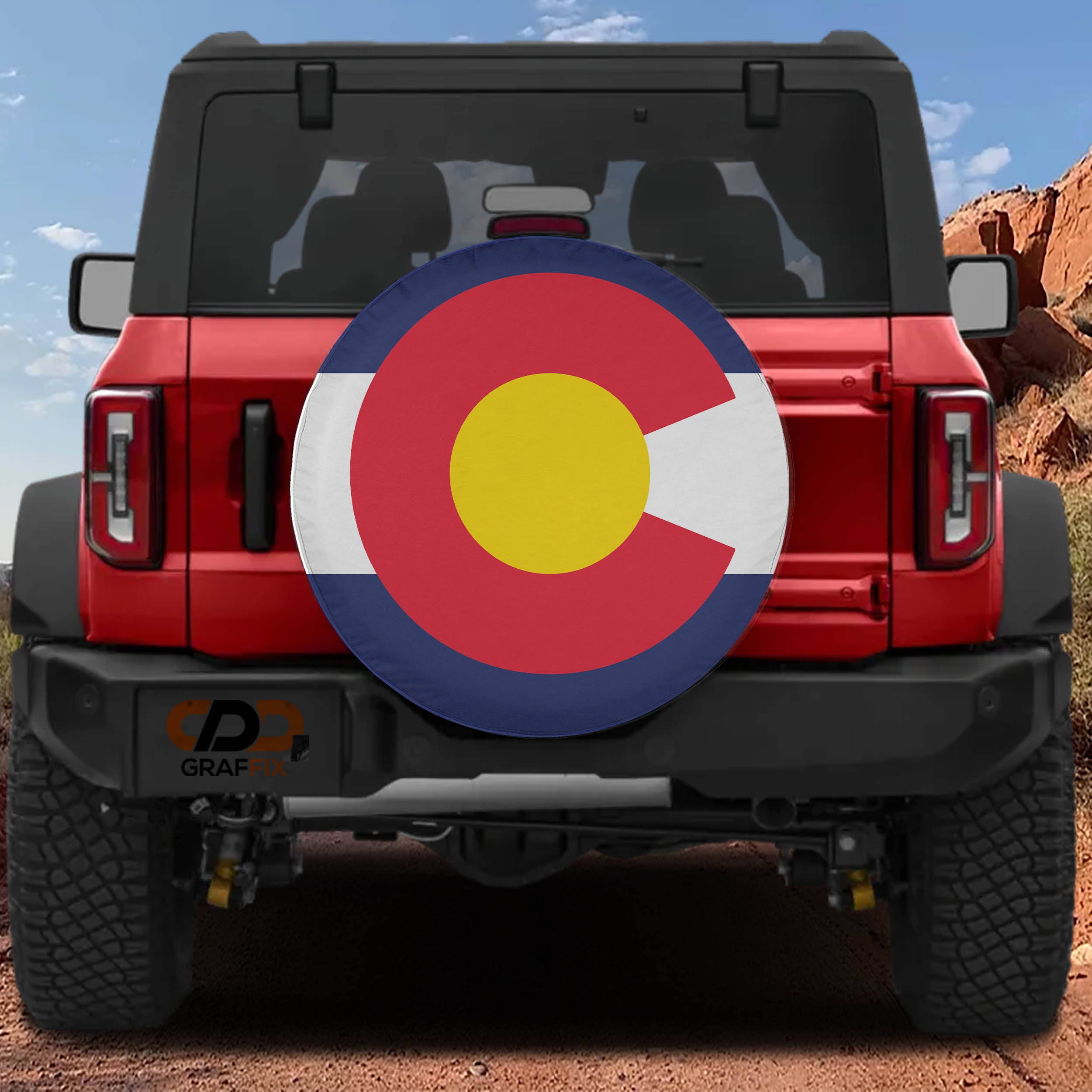 Colorado state flag spare tire cover mounted on red Ford Bronco rear with red rock canyon backdrop