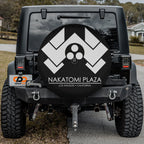 Nakatomi Plaza spare tire cover mounted on black Jeep Wrangler rear with white logo and camera cutout