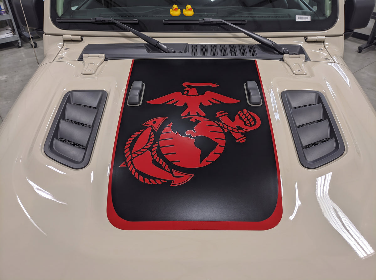 Tan Jeep Wrangler Rubicon hood with a matte black power-dome graphic, red Marine Corps Eagle, Globe and Anchor emblem, and red pinstripe border, two rubber ducks on the cowl