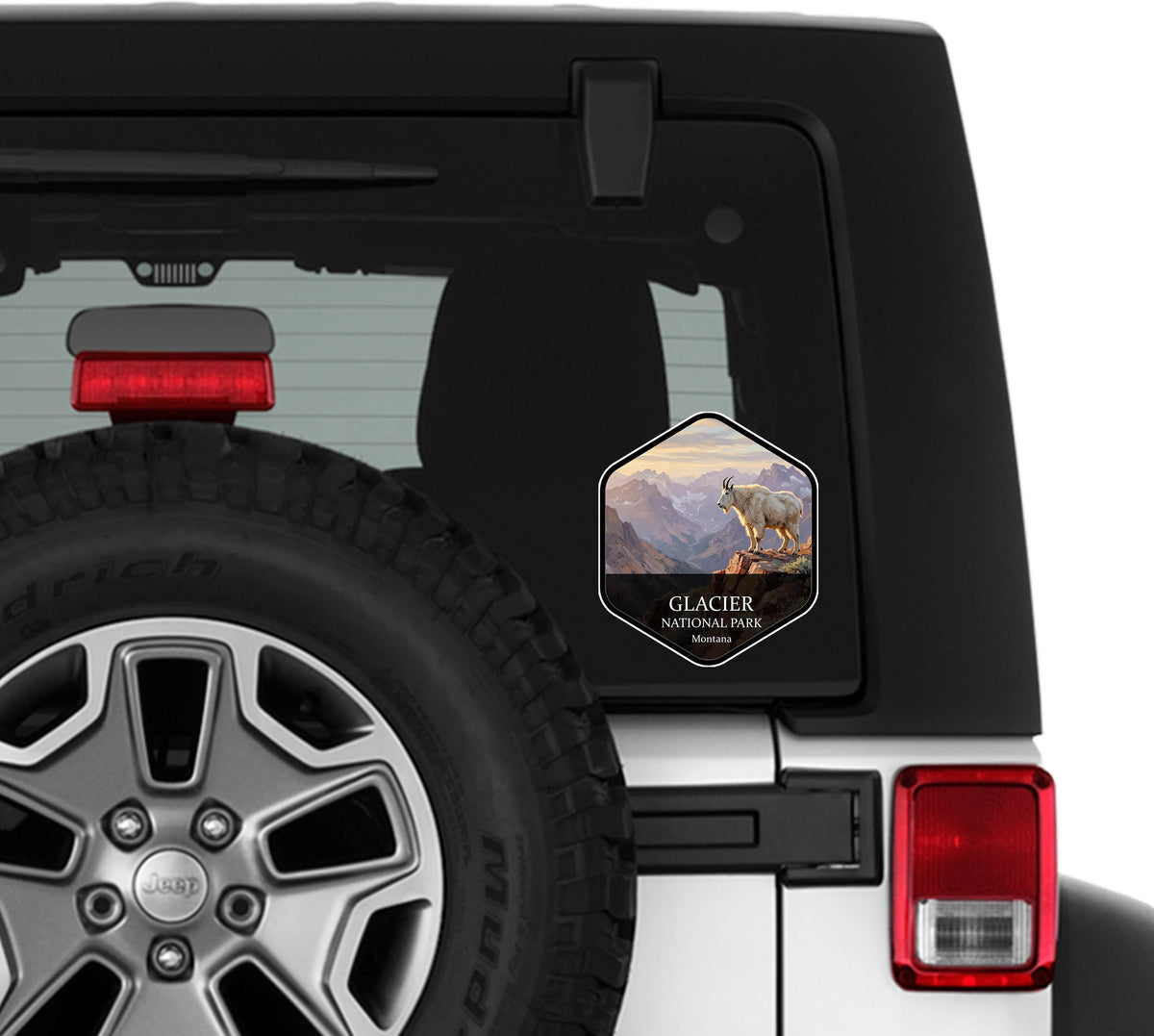 Glacier National Park badge sticker applied to the rear window of a white Jeep Wrangler beside the spare tire