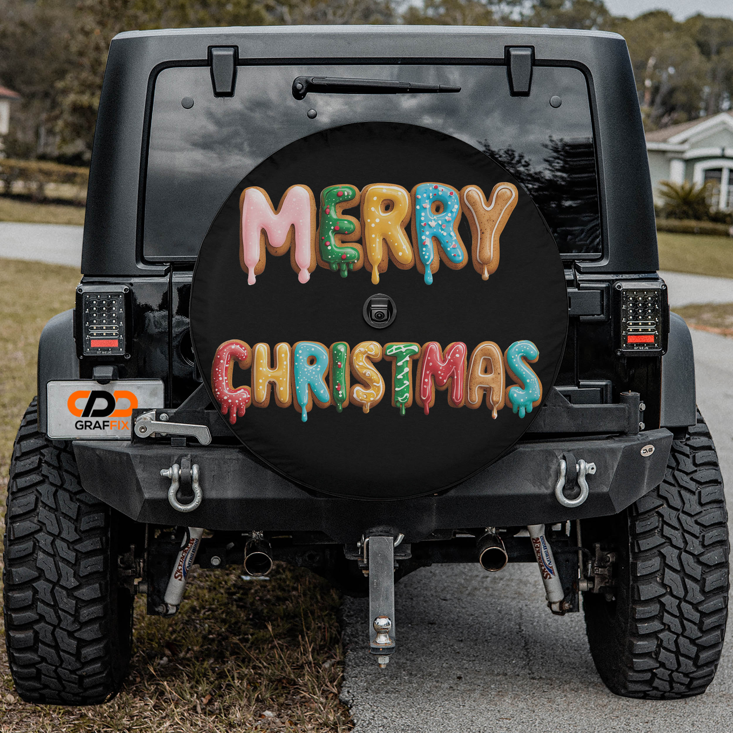 a black Jeep Wrangler with a large, colorful tire cover that says "MERRY CHRISTMAS" in a festive font.