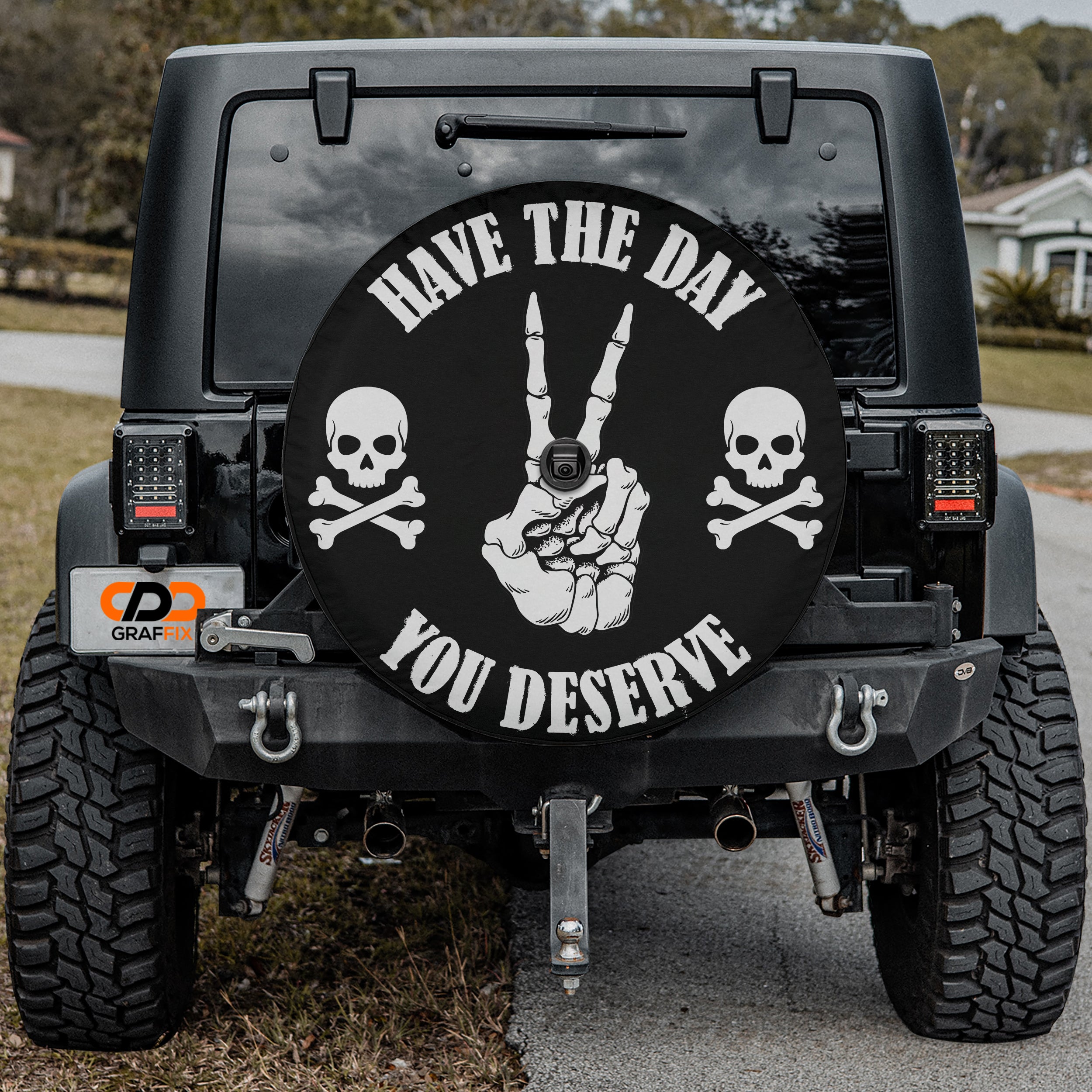 the back of a black Jeep Wrangler with a large black wheel cover featuring a skull and crossbones design and the text "Have the day you deserve".