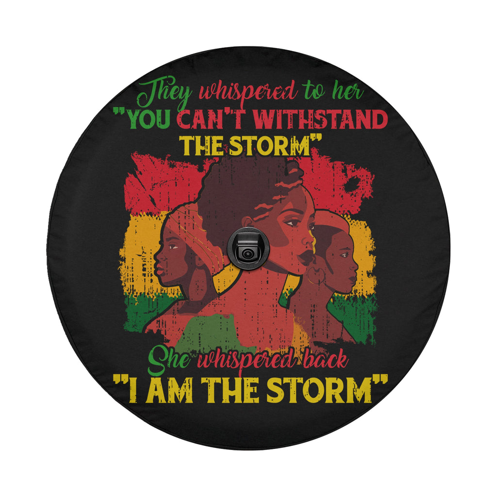 a black wheel cover with a colorful graphic design depicting three stylized female figures. The text on the wheel cover reads "They whispered to her 'YOU CAN'T WITHDRAW THE STORM' She whispered back 'I AM THE STORM'".