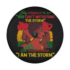 a black wheel cover with a colorful graphic design depicting three stylized female figures. The text on the wheel cover reads "They whispered to her 'YOU CAN'T WITHDRAW THE STORM' She whispered back 'I AM THE STORM'".
