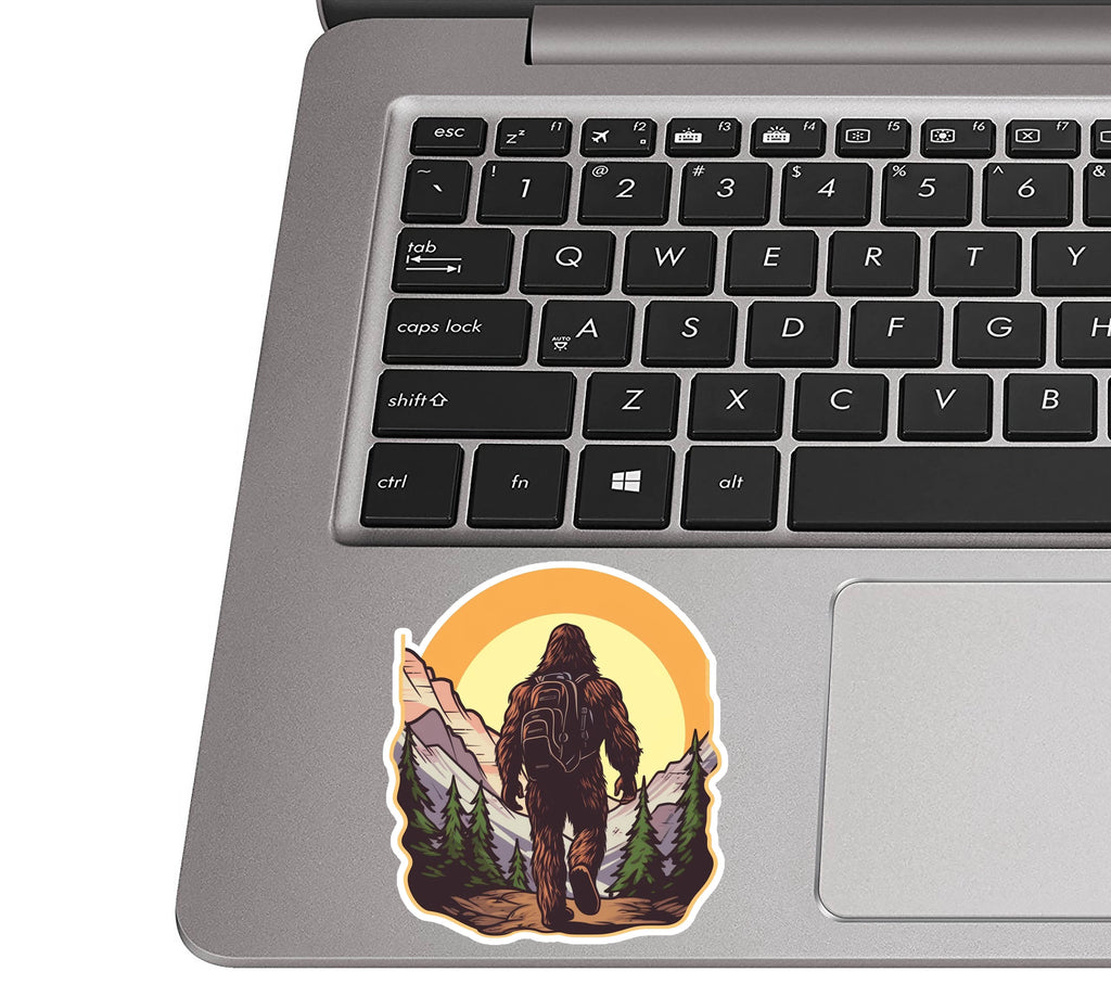 Bigfoot-camping illustration sticker on a silver laptop palm rest beside a black QWERTY keyboard for size